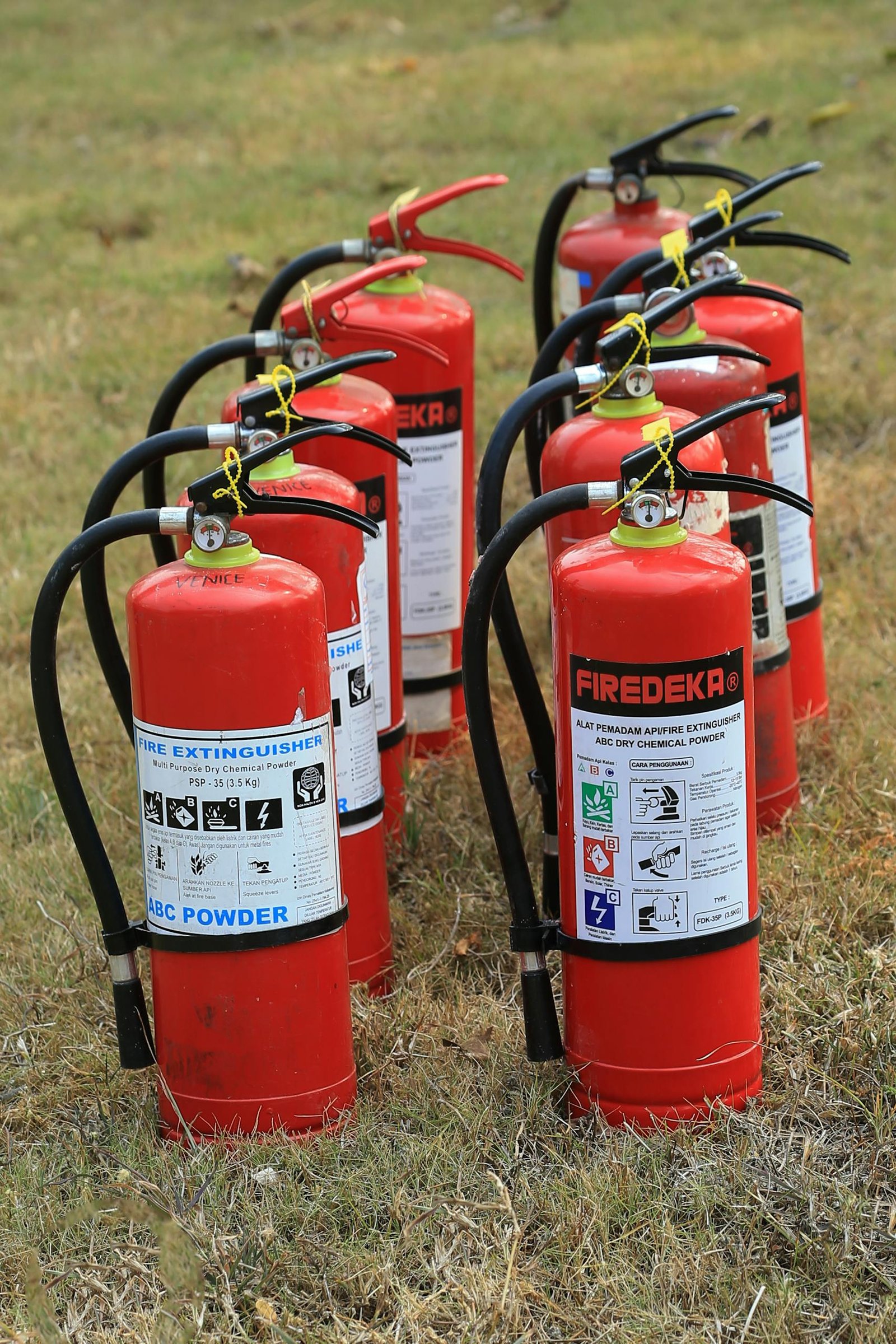 Multiple fire extinguishers lined up on grass, ready for emergency use, showcasing fire safety equipment. Multiple fire extinguishers lined up on grass, ready for emergency use, showcasing fire safety equipment.